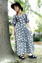 Woman in a black and white patterned boho dress standing next to a tree outdoors.