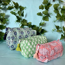 Three boho patterned cylindrical bags with tassels on a light blue background with green leaves.