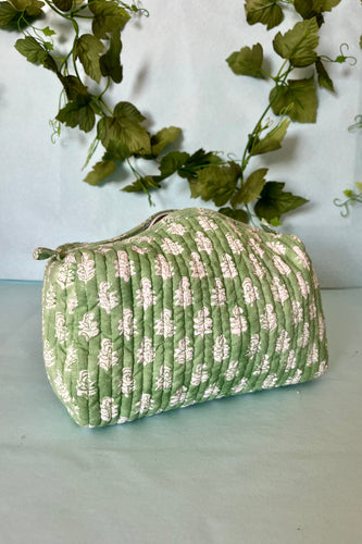 A medium-sized boho toiletries bag with a green and white floral hand block print design, closed with a zipper that has tassel trim.