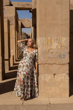 Woman in a boho floral dress standing in front of ancient stone architecture with hieroglyphics.
