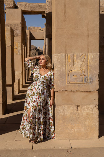 Woman in a boho floral dress standing in front of ancient stone architecture with hieroglyphics.