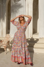 Woman in a colorful dress standing in a sunlit outdoor setting with classical architecture.