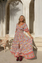 Woman in a colorful boho dress standing in an elegant outdoor setting with arches and tables.