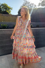 Woman in a boho floral dress standing outdoors with trees and a fence in the background