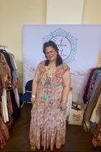 Woman in a boho floral dress standing in front of a clothing store backdrop with racks of clothes on either side.