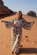 Woman in a boho floral outfit standing in a desert landscape with sand dunes and rock formations.
