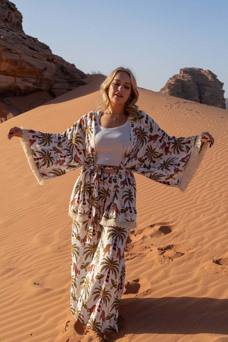 Woman in a boho floral outfit standing in a desert landscape with sand dunes and rock formations.
