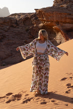 Woman in a boho outfit standing in a desert landscape with rocky formations.