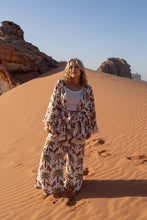Woman in a boho patterned outfit standing on a sand dune in a desert landscape
