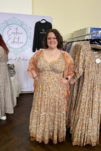 Woman in a floral dress standing next to a rack of dresses in a store.
