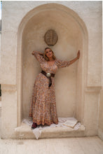 Woman in a floral dress standing in a stone archway with arms outstretched.