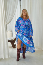 A woman modeling a blue floral boho maxi dress with balloon sleeves and a V-neckline, paired with brown boots.