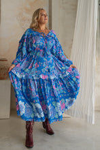 A woman modeling a blue floral boho maxi dress with balloon sleeves and a V-neckline, paired with boots.