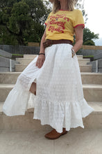 Person wearing a yellow shirt and white boho skirt standing on steps outdoors.