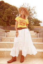 Woman in a yellow top and white skirt standing on stone steps outdoors.