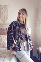 Woman sitting on a bed in a bedroom wearing a boho floral kimono-style jacket.
