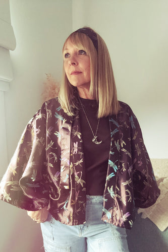 Person wearing a boho floral jacket over a dark top and light jeans indoors.