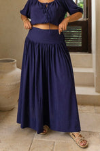 Person wearing a boho navy blue top and long skirt standing in a sunlit outdoor setting.