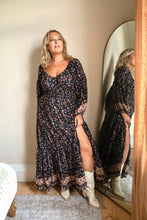 Woman wearing a floral boho dress with a slit standing in front of a mirror.