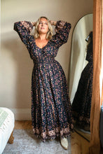 Woman in a floral boho dress standing in front of a mirror in a room.