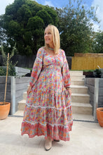 Woman in a colorful b boho floral dress standing outdoors with trees and steps in the background