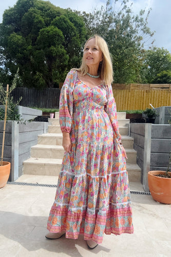 Woman in a boho colorful dress standing outdoors on a patio with plants and steps in the background.