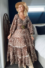 Woman in a boho leopard print dress and hat standing in a bedroom.
