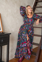 Woman in a colorful floral boho dress standing on a staircase.