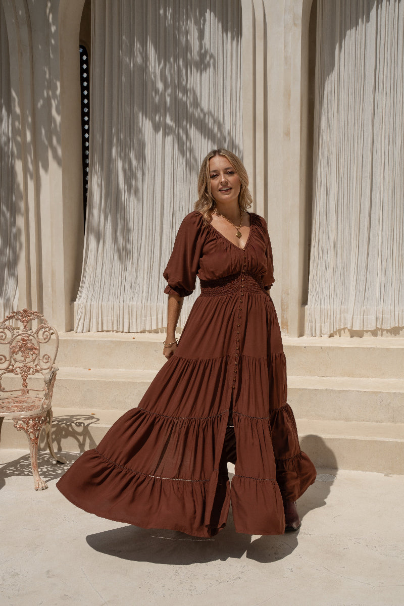 Woman in a boho brown dress standing in front of a classical building with columns.