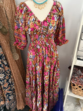 Floral boho dress on a mannequin against a white wall with shelves in the background.