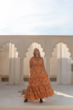 Woman in an orange boho floral dress standing in front of arched architectural elements.