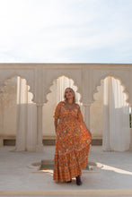 Woman in a boho floral dress standing in front of arched stone walls with a clear sky.