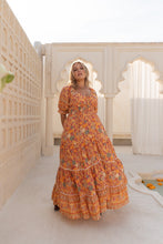 Woman in an orange floral boho dress standing in a sunlit architectural setting