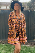 Woman wearing a boho floral dress and black hat outdoors