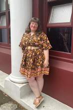 Woman in a floral boho dress standing outside a building with columns.