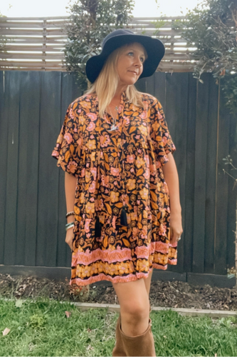 Woman wearing a boho floral dress and black hat outdoors