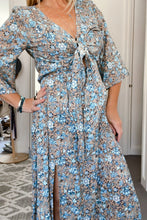 Woman wearing a floral boho dress with a pattern of blue flowers on a neutral background