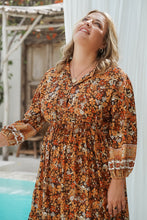 Woman wearing a floral boho dress standing outdoors near a white wall.