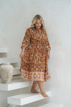 Woman in a floral dress standing on white steps with a white wall background