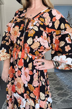 Person wearing a black floral boho dress with colorful flowers indoors.