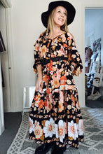 Woman wearing a floral boho dress and black hat indoors.
