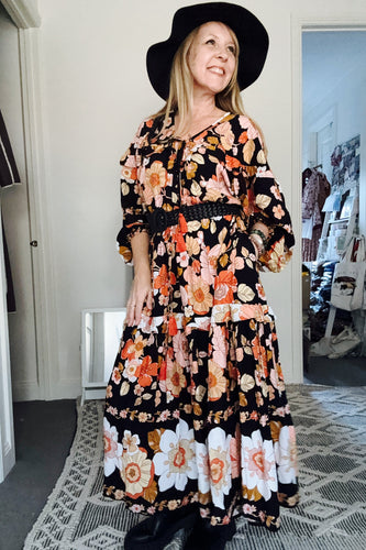 Woman wearing a floral boho dress and black hat indoors.