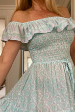 Woman wearing a light green patterned dress with ruffled sleeves.