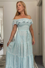 Woman wearing a light blue off-shoulder dress in a room.