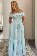 Woman wearing a light blue off-shoulder dress in a room with a neutral background