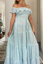 A woman wearing an off-the-shoulder, floral maxi dress with a ruffled bodice and a tiered skirt.