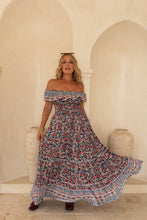 Woman wearing a floral off-shoulder dress in a decorative interior setting.