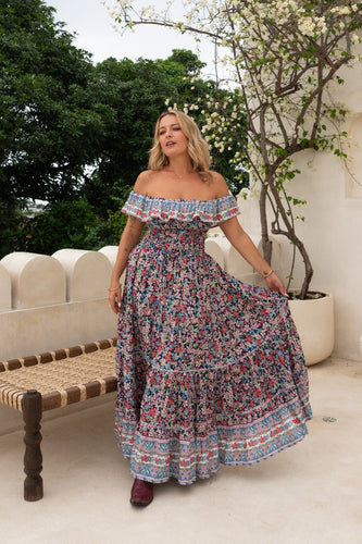 Woman in a boho floral off-shoulder dress standing outdoors with greenery in the background
