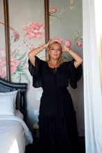 Woman in a black dress standing in a bedroom with floral wallpaper.