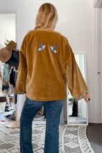 Person wearing a mustard yellow boho jacket with bird designs in a room.
